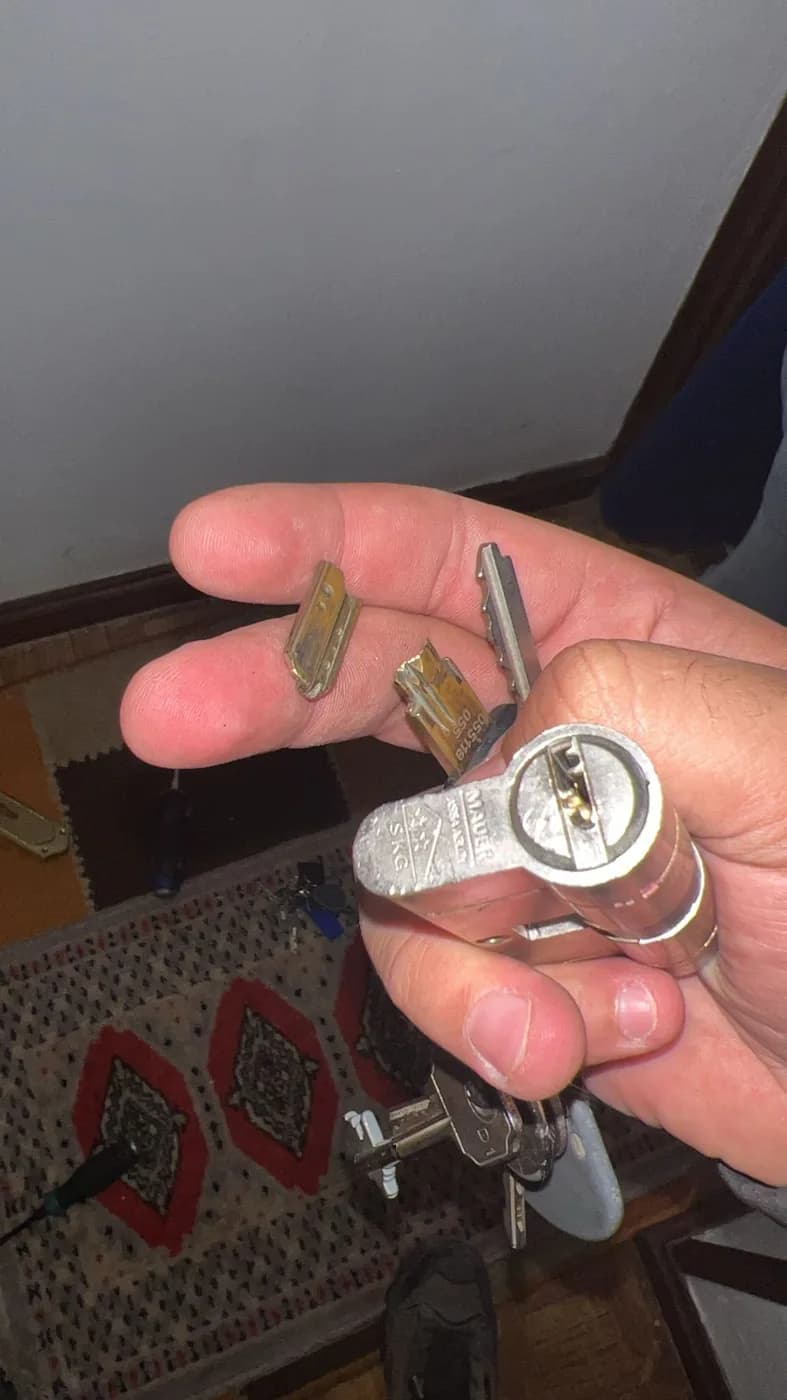 Bombín de alta seguridad con marcado de certificación sostenido en la mano, junto a llaves de perfil dentado
