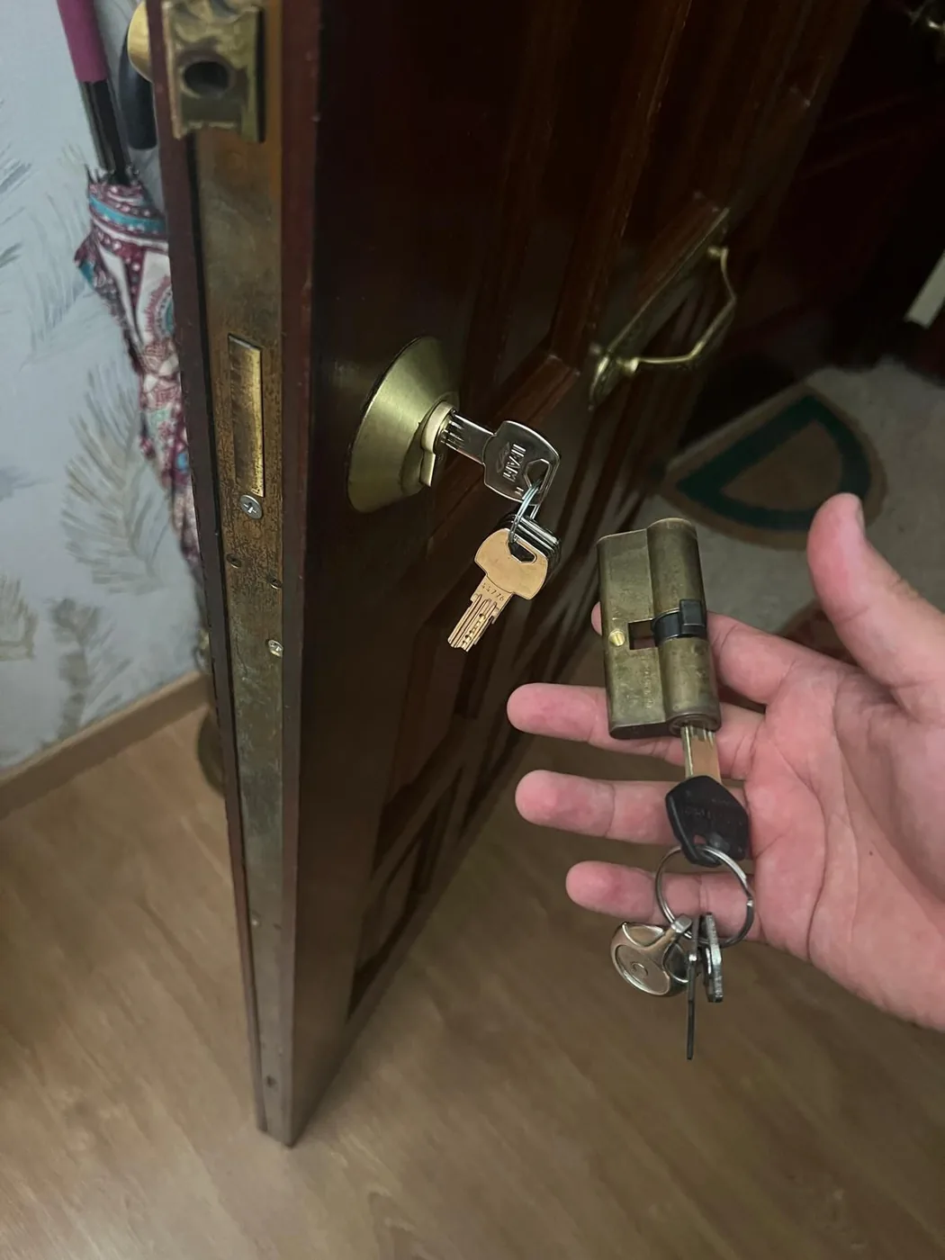 Bombín antiguo de latón ya extraído sostenido en la mano, con la puerta de la vivienda abierta y la llave puesta en el pomo