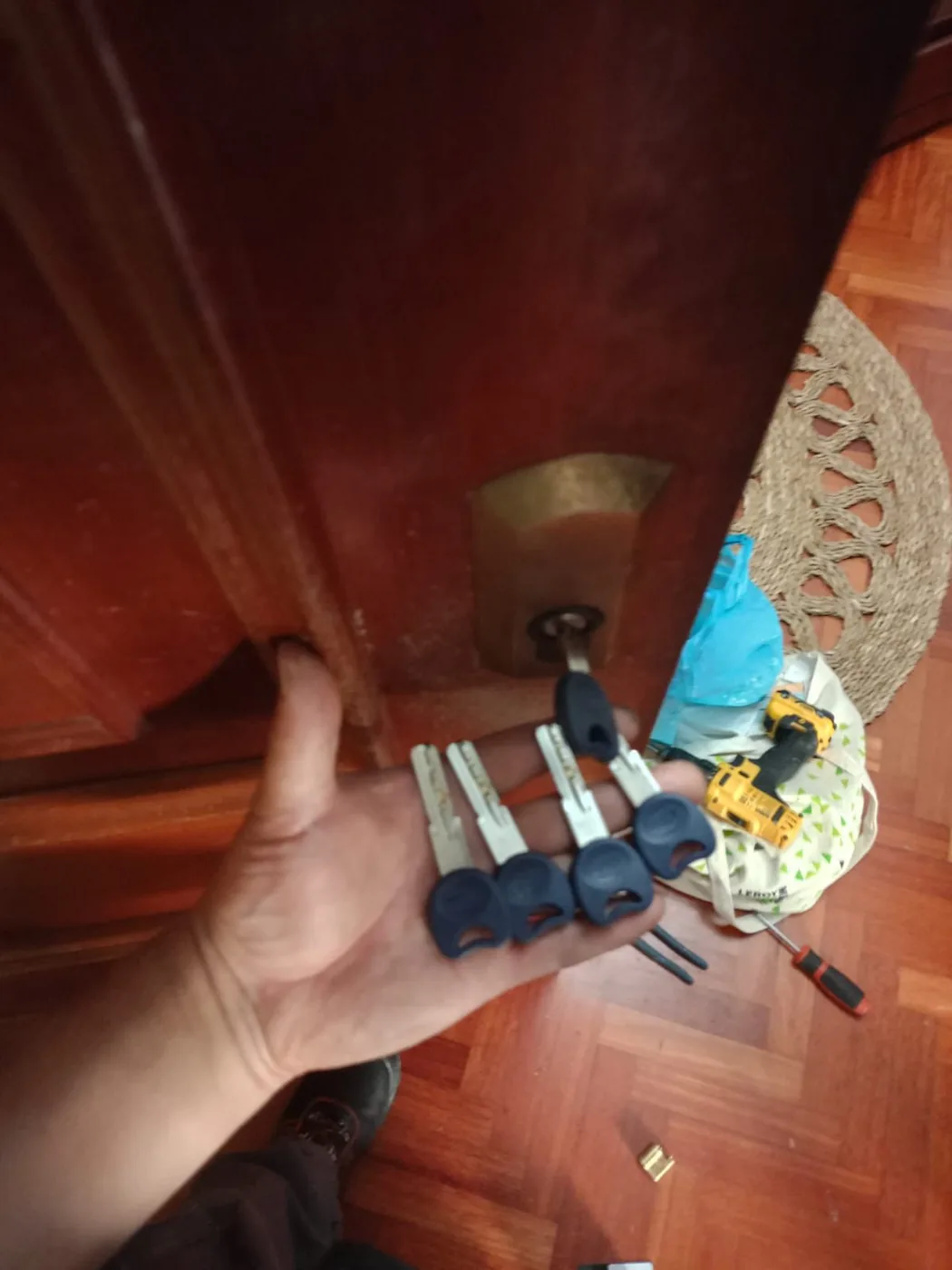 Mano sosteniendo cinco llaves nuevas de seguridad recién entregadas, con herramienta de trabajo al fondo