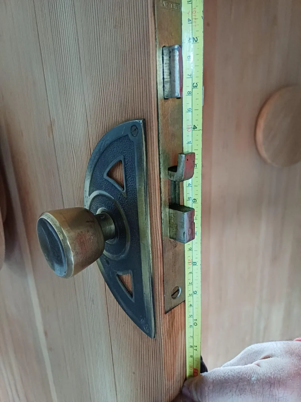 Cerrajero midiendo con un flexómetro la cerradura embutida de una puerta antigua con pomo de latón