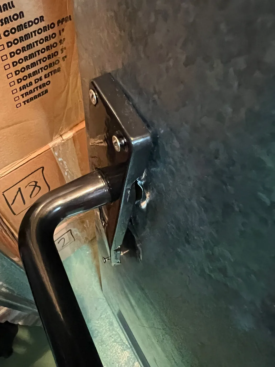 Detalle de la manilla y la placa de una puerta metálica con el marco marcado a la altura del cerradero