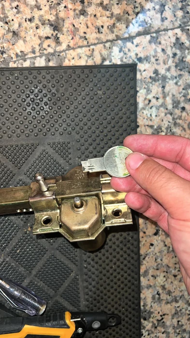 Cerradura de sobreponer desmontada sobre un felpudo, con su llave de gorja plana y un destornillador al lado